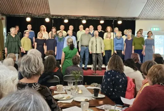 Kören på scenen på Oasen i Hågaby, med publik vid borden framför.